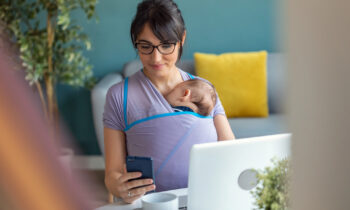 A mom with a baby in a sling searching for virtual part-time jobs on her laptop