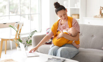 A young mom with her baby in a sling working her side hustle from home