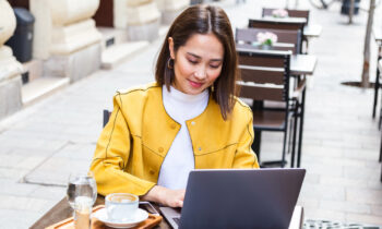 A Young woman in a yellow jacket working on laptop searching for remote non-phone jobs